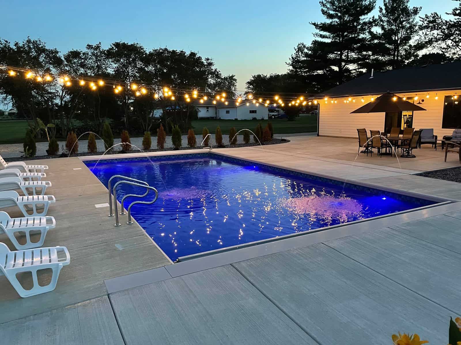 A pool with chairs and string lights at dusk.
