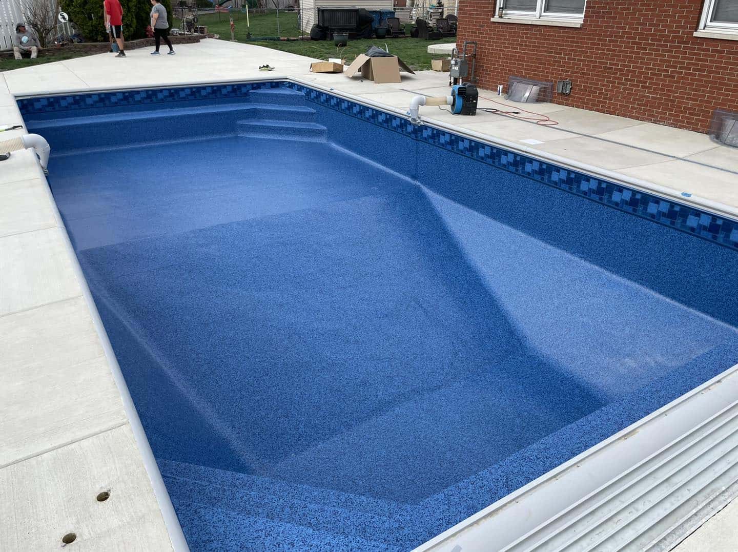A blue swimming pool is being installed in a backyard.