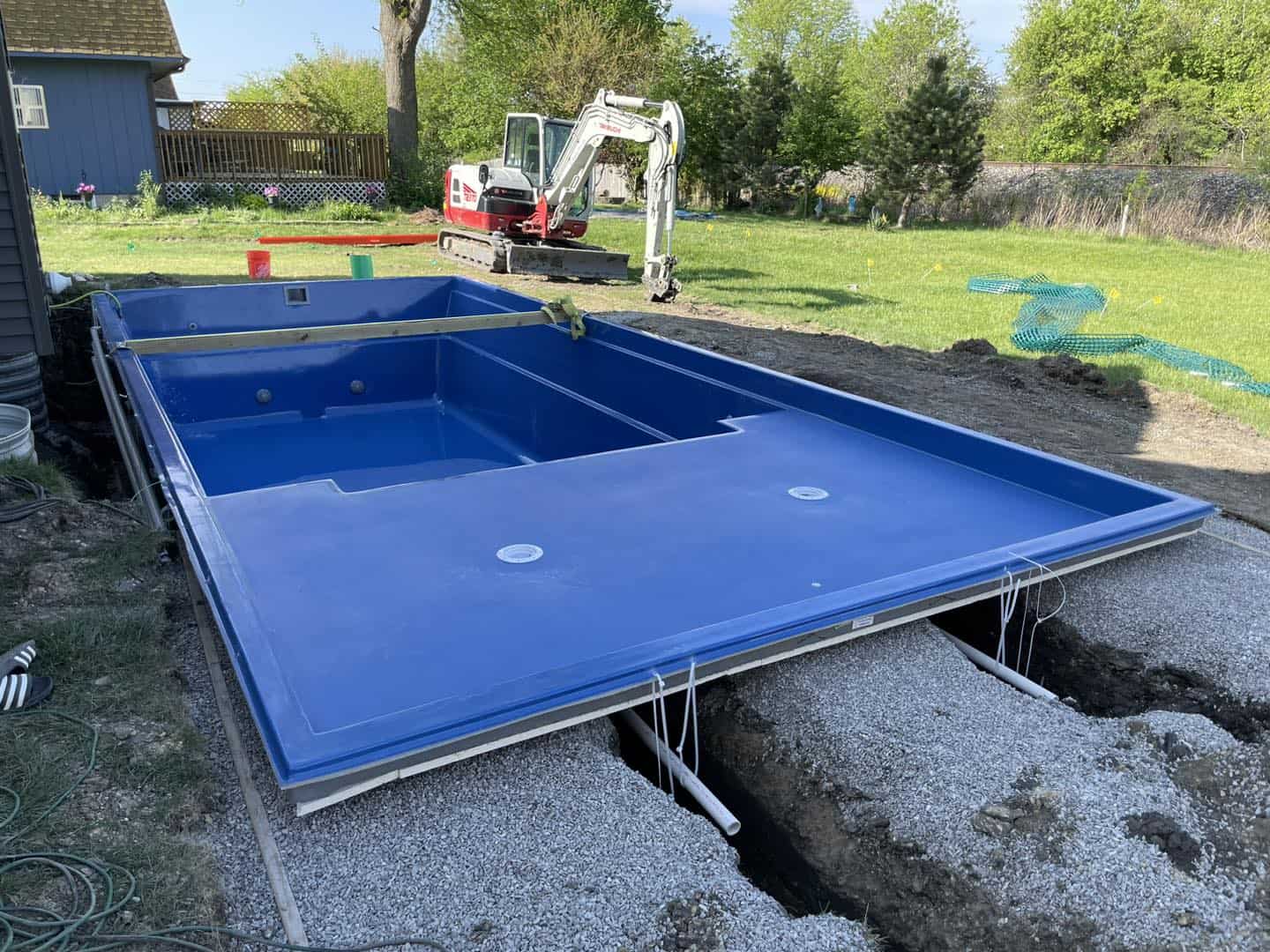 A blue swimming pool is being built in a backyard.