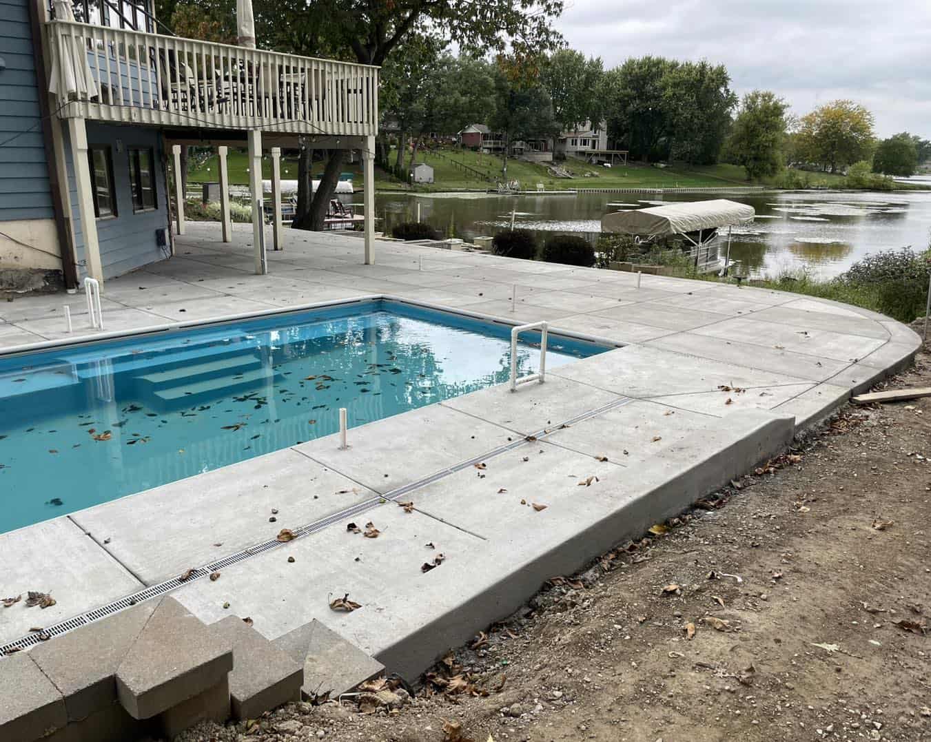 A concrete pool with a deck next to a lake.