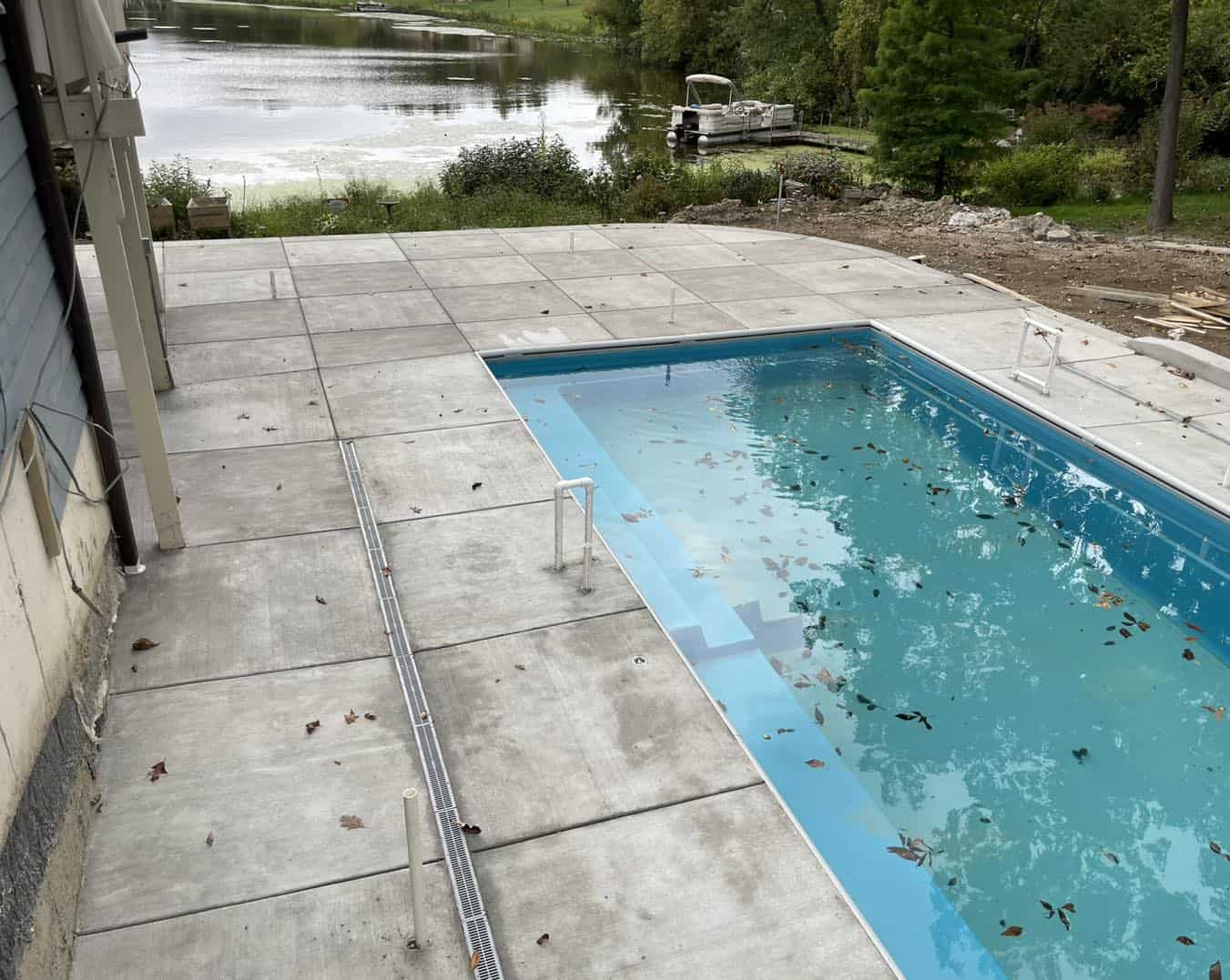 A concrete pool in a backyard next to a lake.