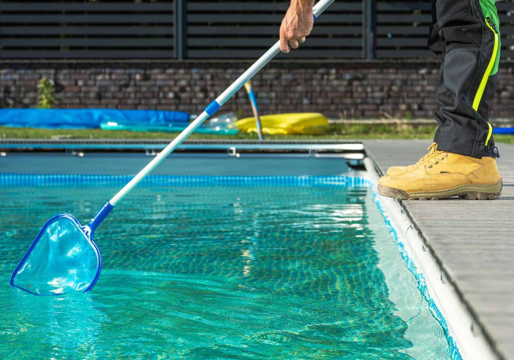 Caucasian Professional Pool Worker with a Pool Net Cleaning Residential Outdoor Swimming Pool